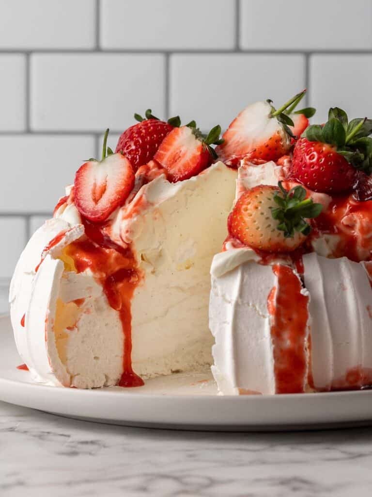 A baked meringue with fresh strawberries and cream with a slice taken out