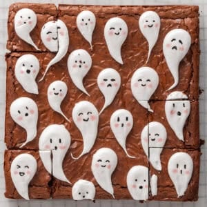A brownie cut into squares, decorated with white icing ghosts featuring various hand-drawn faces.
