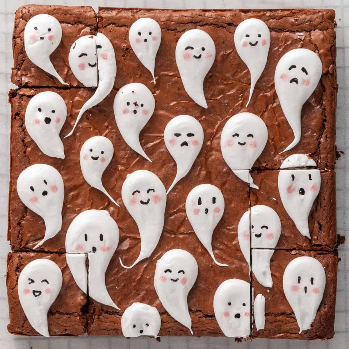 A brownie cut into squares, decorated with white icing ghosts featuring various hand-drawn faces.