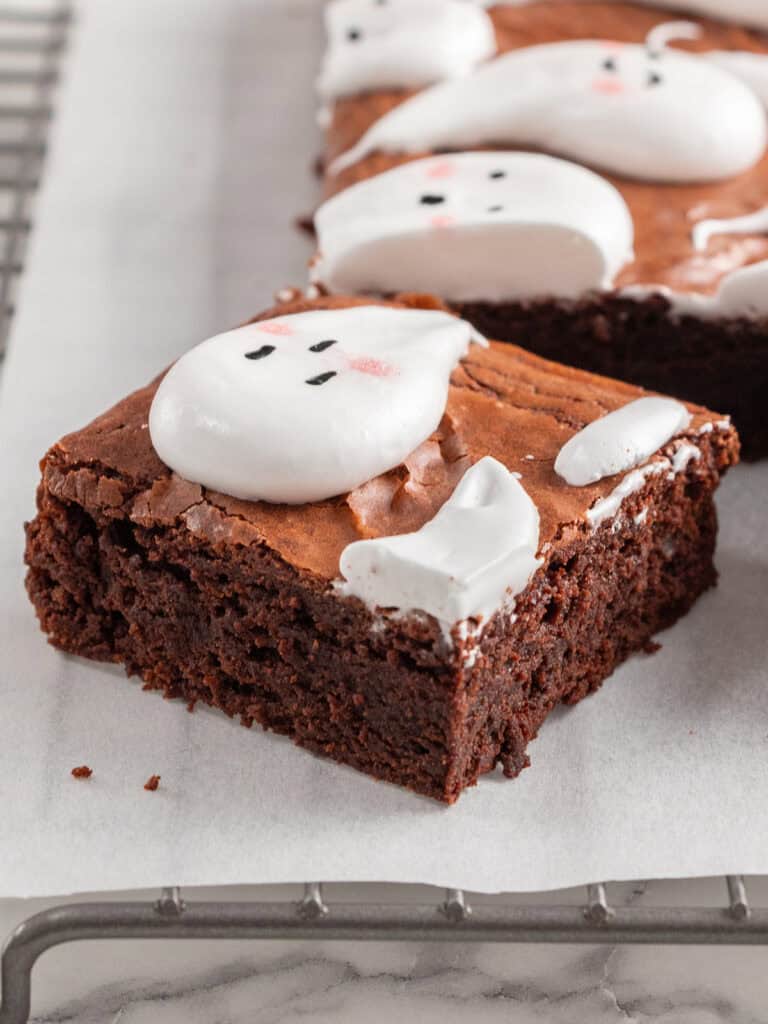 Chocolate brownies topped with ghost-shaped marshmallows decorated with black eyes and pink cheeks.
