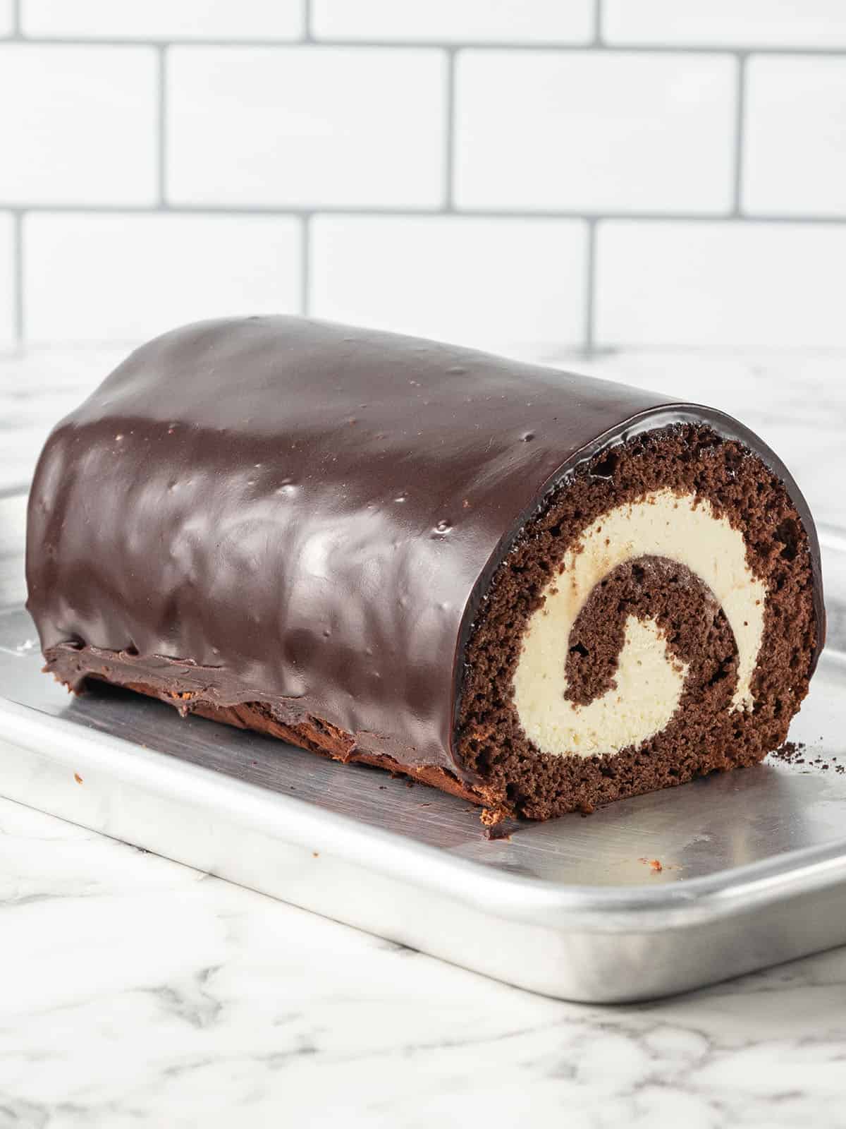 Chocolate Swiss Roll Cake - swiss roll sitting on a baking tray covered in sauce