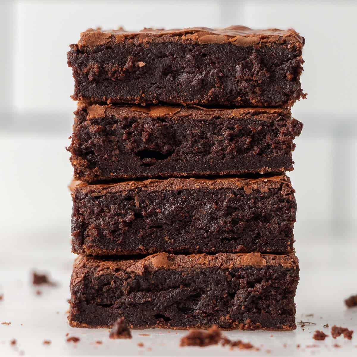 Square image of a stack of four chocolate brownies sitting on a benchtop