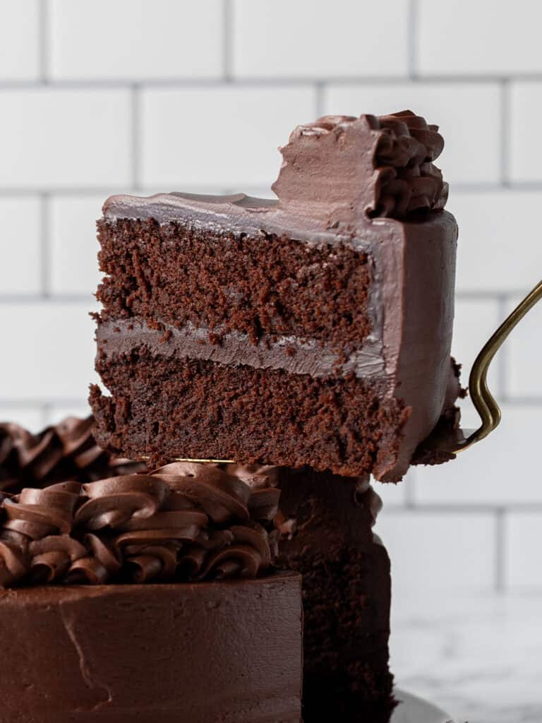 A spatula holding a very moist looking chocolate cake layered with ganache