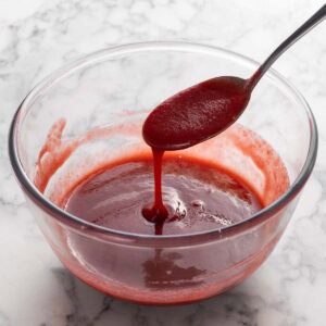 Square image of sauce running off a spoon into a glass bowl