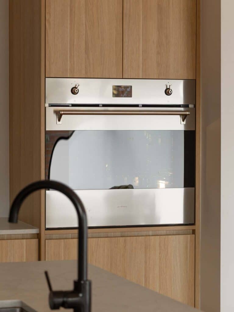 A side shot of an oven in an oven tower with soft glossy lighting and a black tap in the way