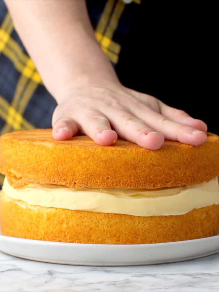 Adding the final layer of cake sponge to finish layering the cake