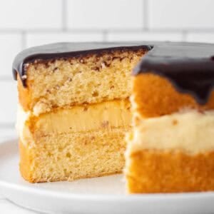 A square image of a vanilla sponge with custard in the centre and chocolate topping on top sliced in half