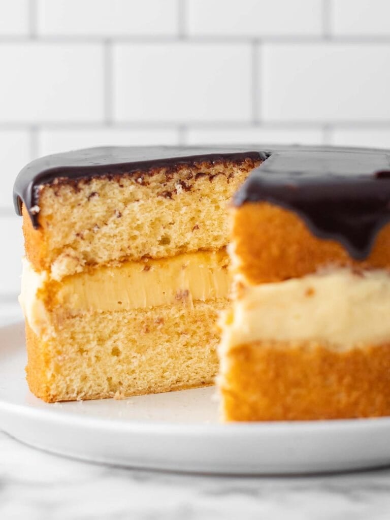 A close up of a vanilla sponge with custard in the middle and chocolate sauce on top