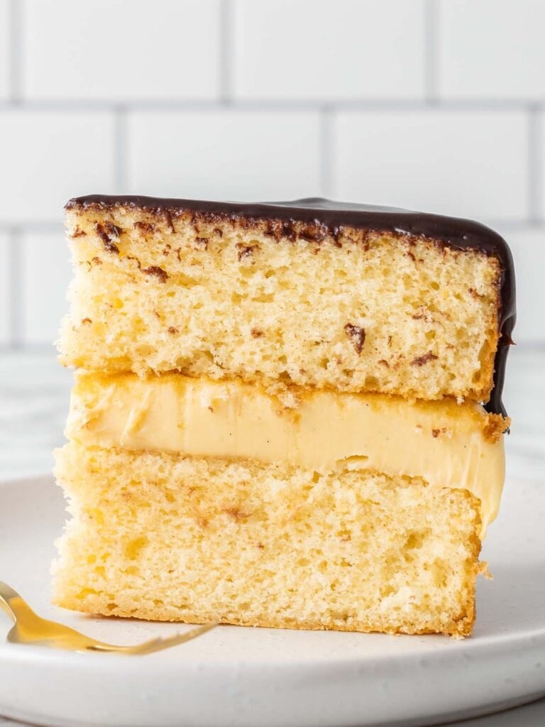 A single slice of vanilla sponge with custard and chocolate on top sitting on a plate