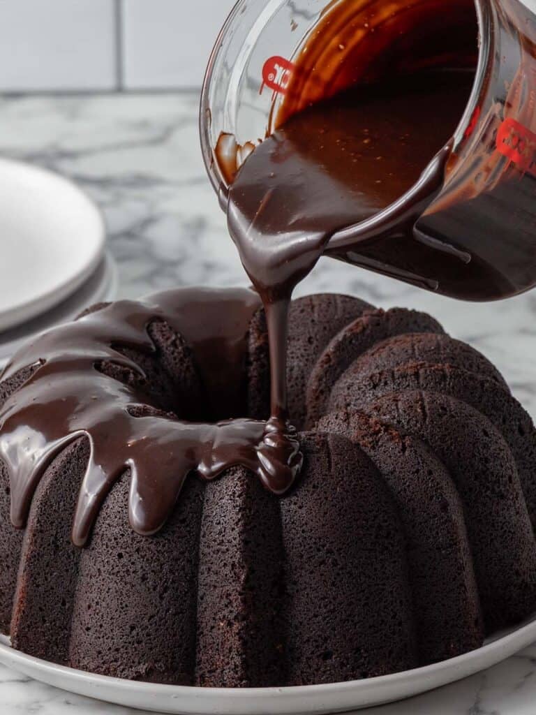 Fudge sauce being poured on top of a chocolate cake