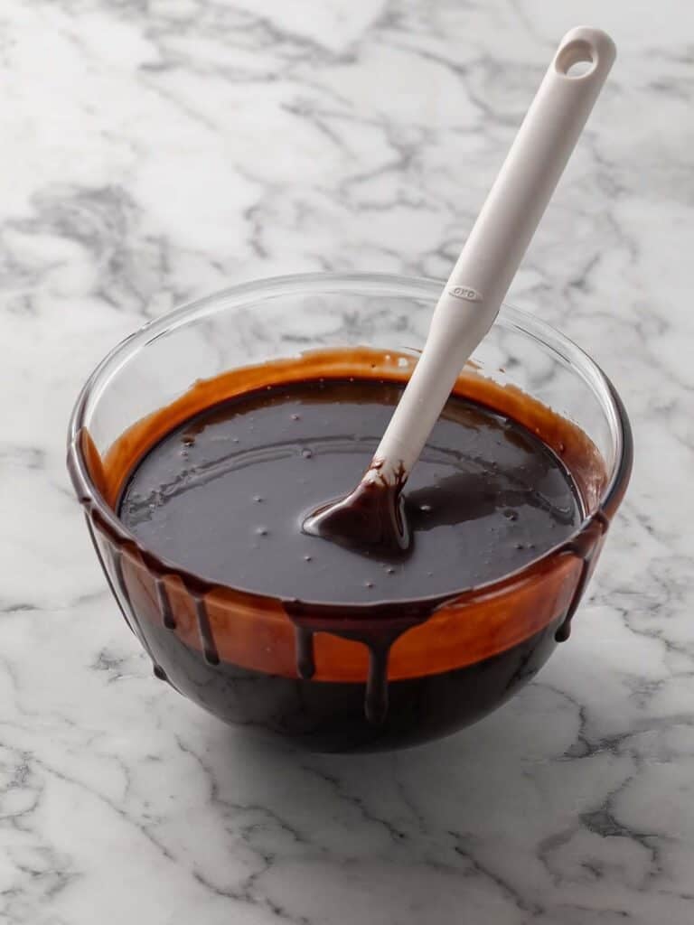 A bowl of glossy fudge sauce with a spatula coming out of it
