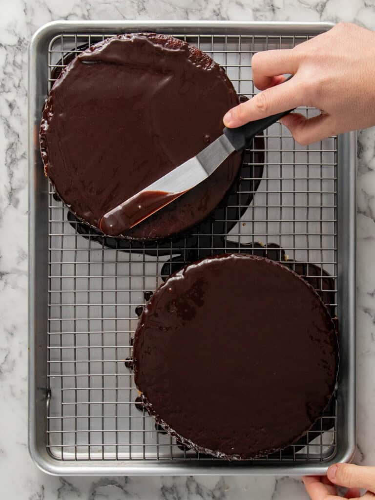 Spreading chocolate glaze on a raspberry vanilla chocolate cake