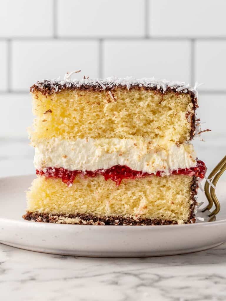 A single slice of chocolate covered vanilla cake filled with cream and raspberry jam covered in coconut