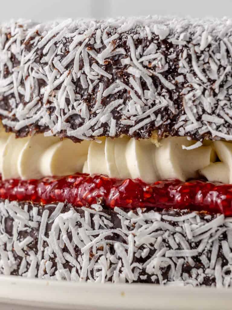 An extreme close up of a chocolate covered vanilla cake filled with cream and raspberry jam