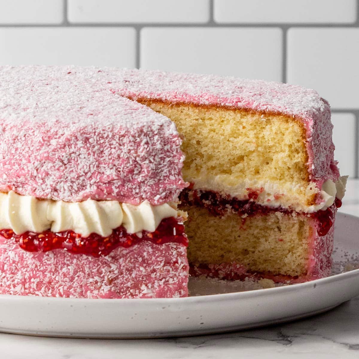Square image of a pink covered sponge cake with jam and cream taken from the front with a slice taken out
