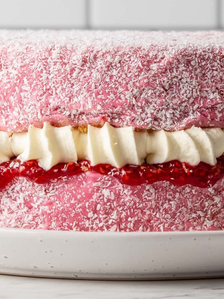 A front on close up shot of a pink covered sponge cake with jam and cream showing the glaze, cream and piped jam
