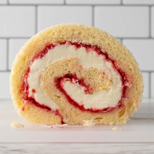 Square front on shot of a spiral log cake filled with chantilly cream and raspberry jam