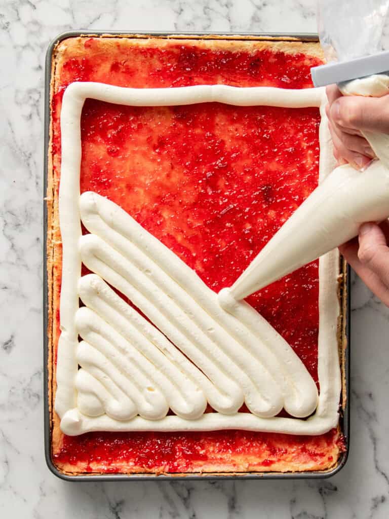 Piping the cream on top of the raspberry filled sponge cake