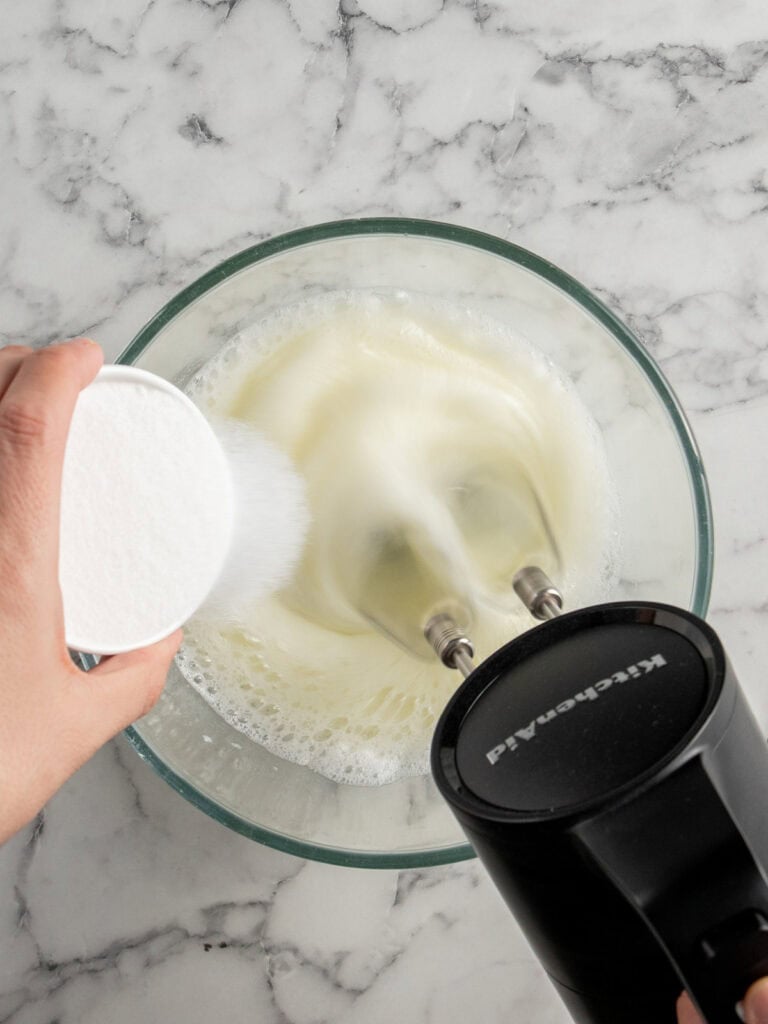 Slowly adding the sugar to the egg whites while the mixer is on high speed
