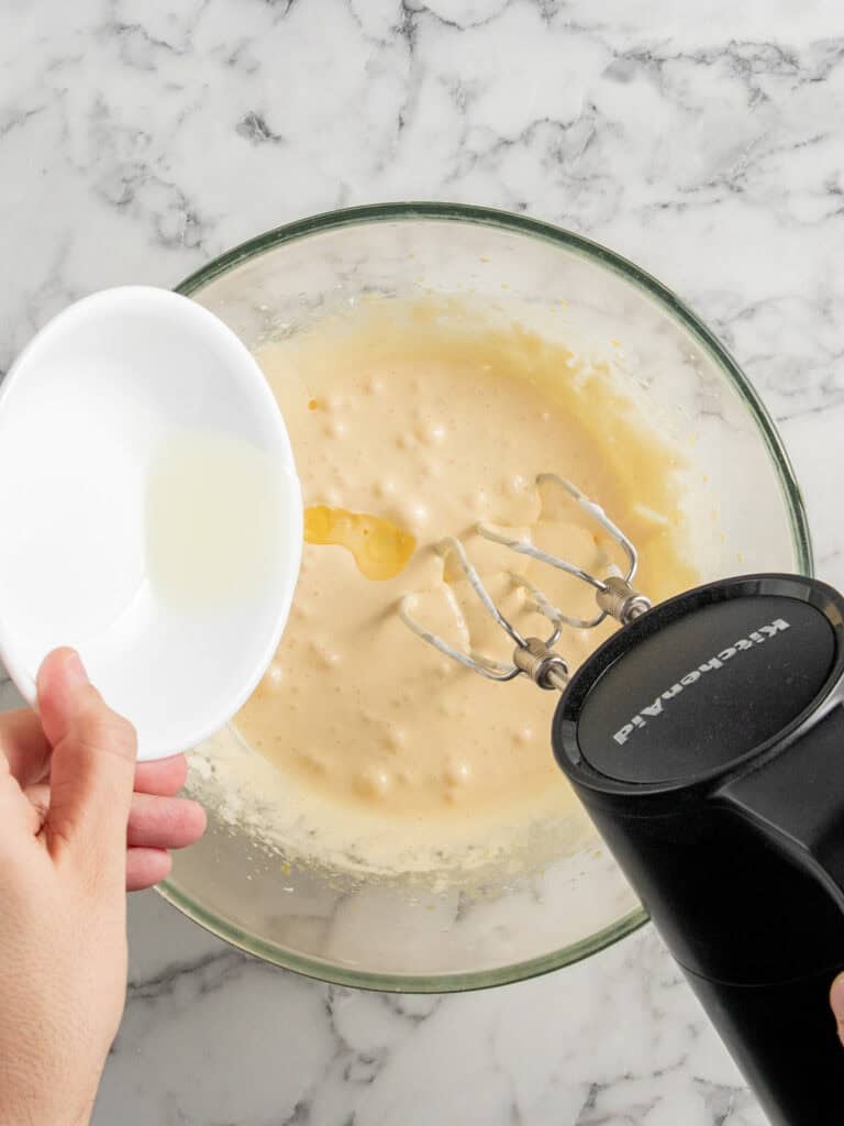 Slowly adding the vegetable oil to the egg yolks mixture while mixing