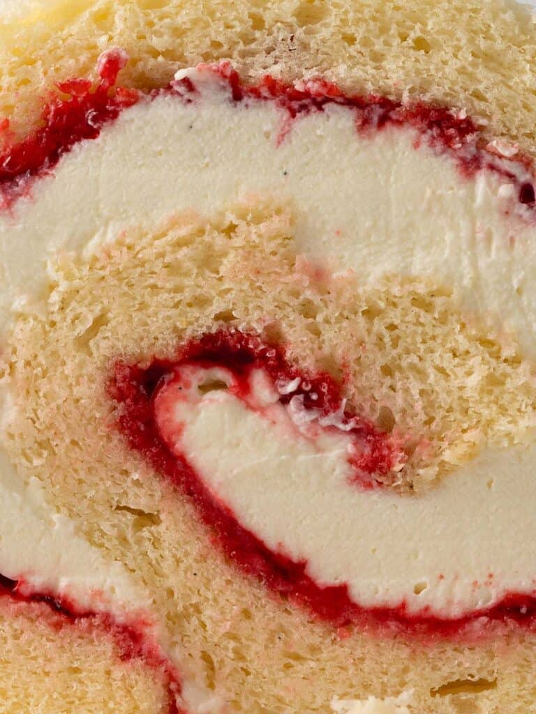 An extreme close up shot of a spiral log cake filled with chantilly cream and raspberry jam