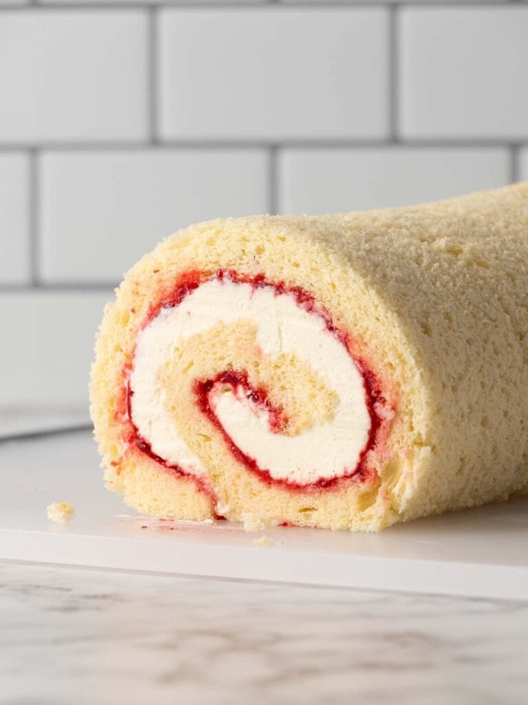 A close up side shot of a spiral log cake filled with chantilly cream and raspberry jam showing the spiral