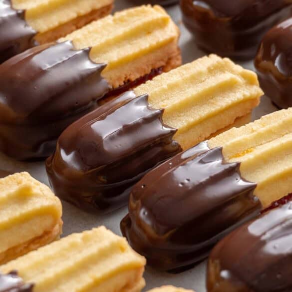 Square close up image of chocolate and jam covered piped biscuit cookies looking ultra glossy