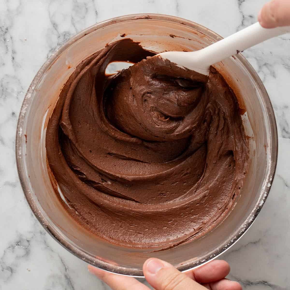 Square image of frosting in a mixing bowl with a white spatula