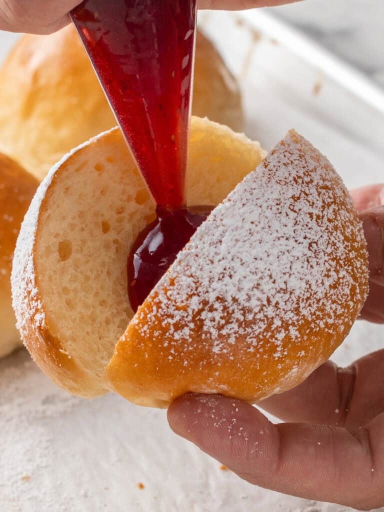 Piping a dollop of raspberry jam in the sliced bun