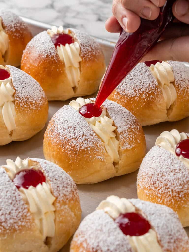 Piping some raspberry jam in the divot to finish the cream buns