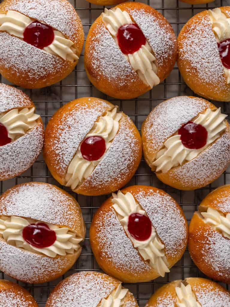 Top down shot of brioche buns with Chantilly and raspberry jam sitting in different directions on a cooling rack