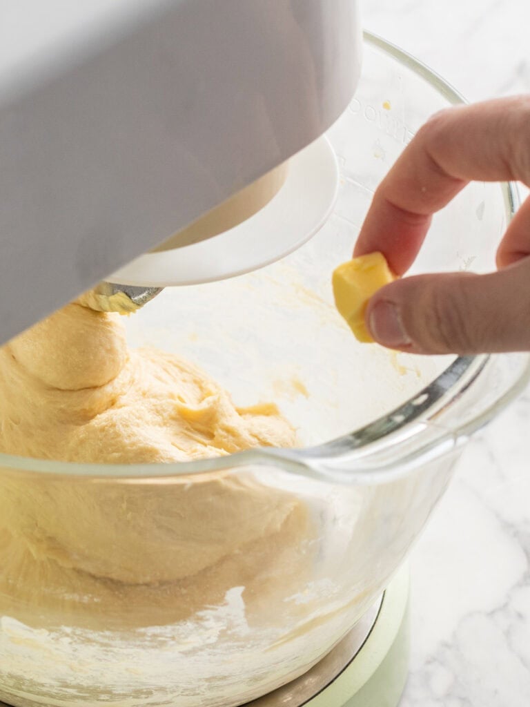 Adding the softened butter to the dough one cube at a time