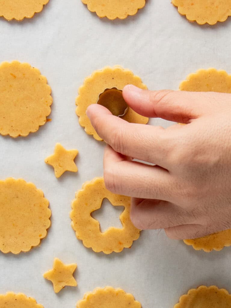 Using a smaller cookie cutter to cut out a window in the middle of half of the cookies