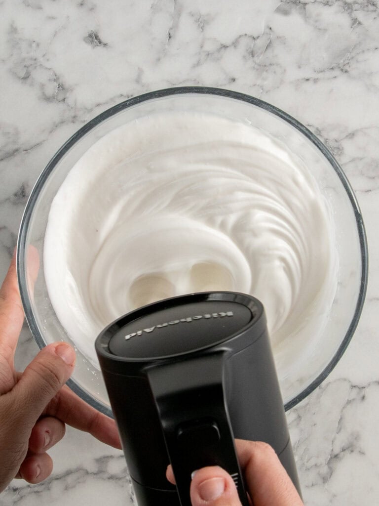 Slowly adding the sugar to the egg whites and whisking until thick and glossy