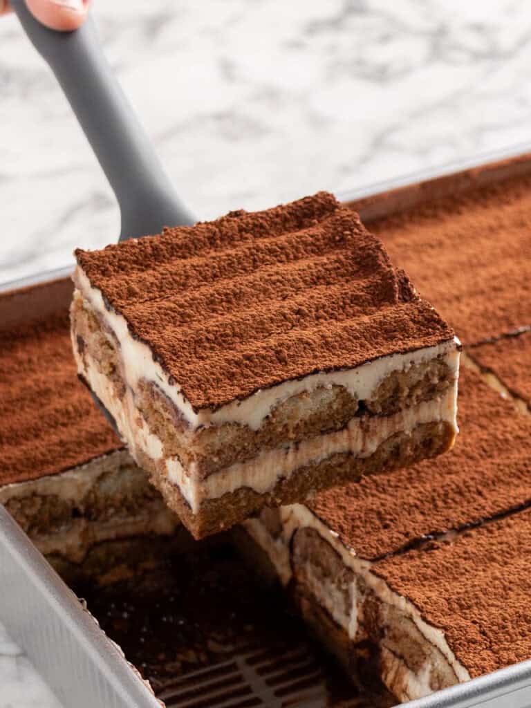 An Italian layered coffee and cream dessert sitting on a spatula above the rest of the dessert