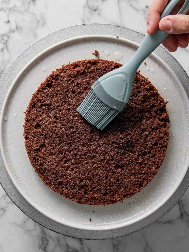 Brushing the first layer of sponge with simple syrup that has cherry brand in it
