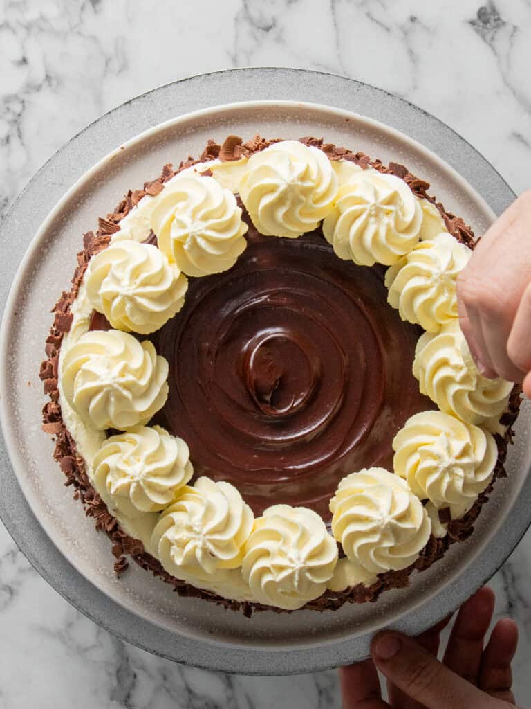 Piping swirls of Chantilly cream on top of the cake