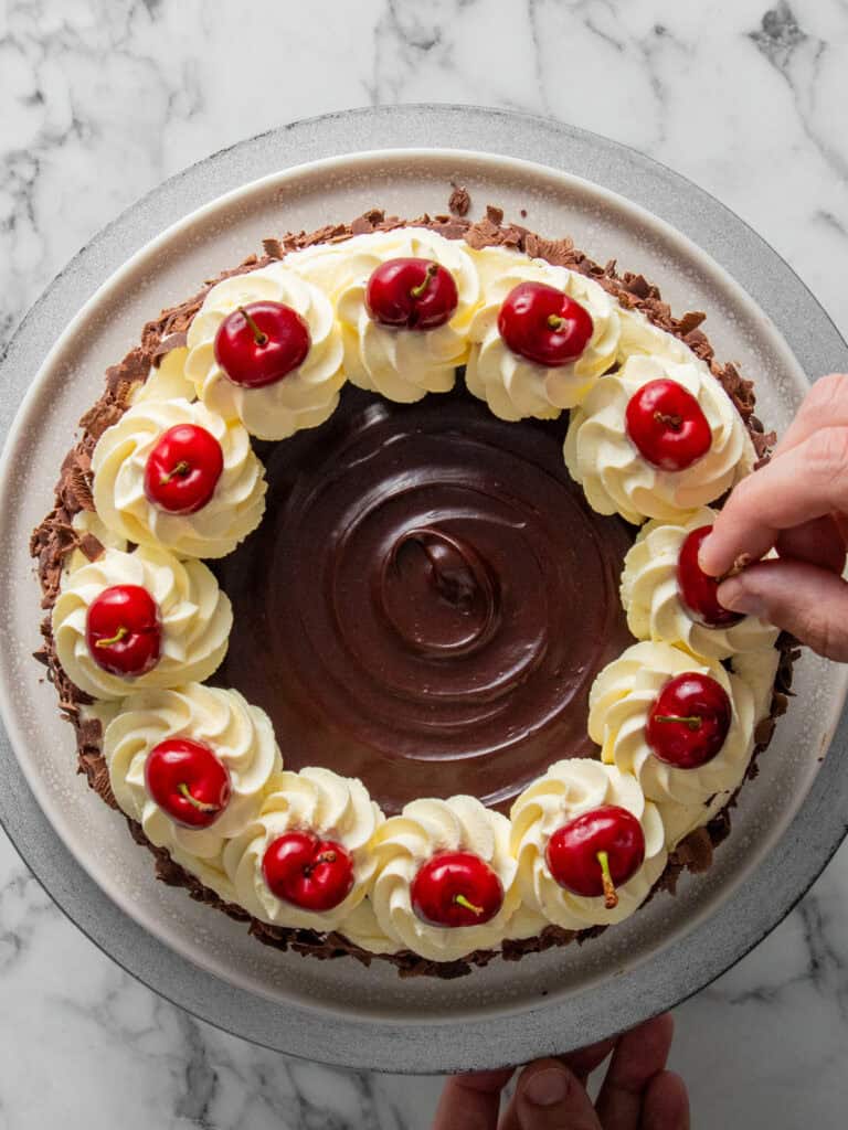 Adding fresh cherries to the top of the cake to finish decorating.