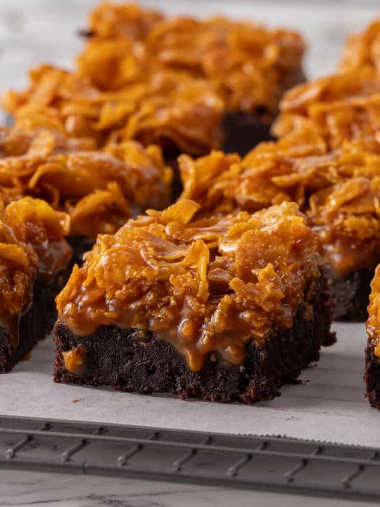 A bunch of crispy caramel topped brownie bars sitting on a cooling rack