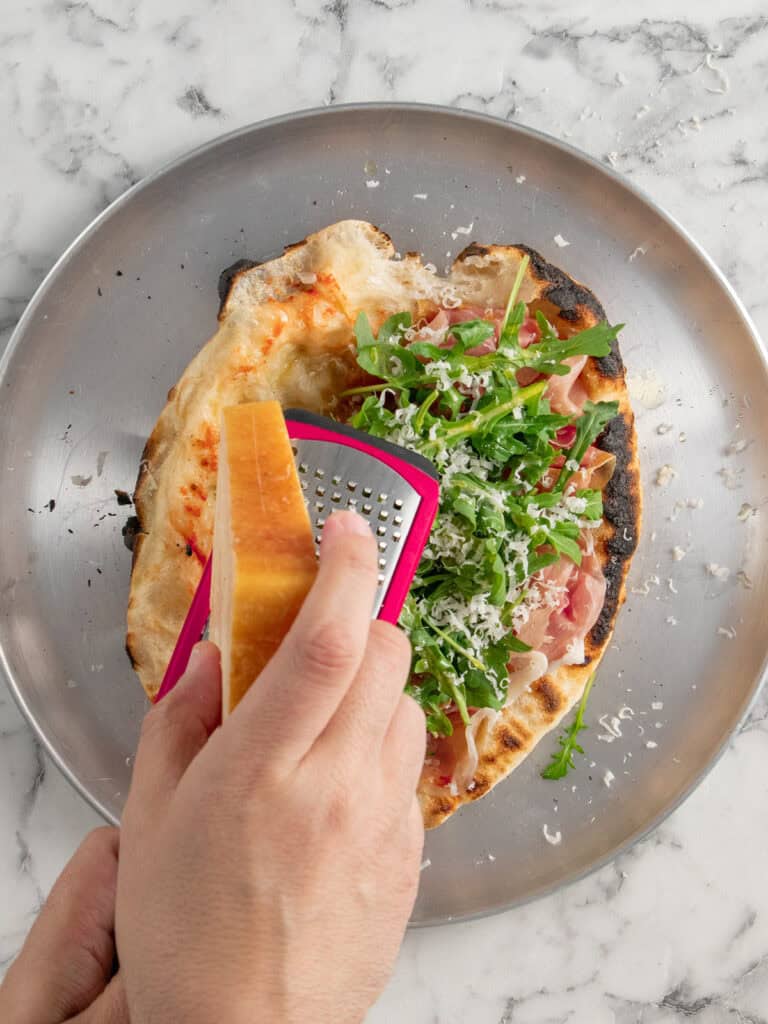 Grating parmesan cheese on top of the calzone
