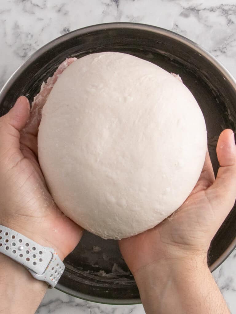 Two hands holding a nice smooth dough ball after kneading