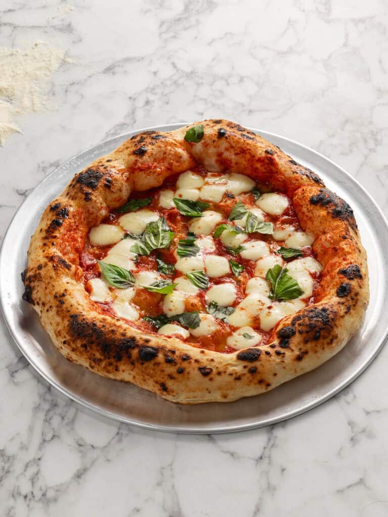 A side shot of a charred looking pizza with cheese and sauce