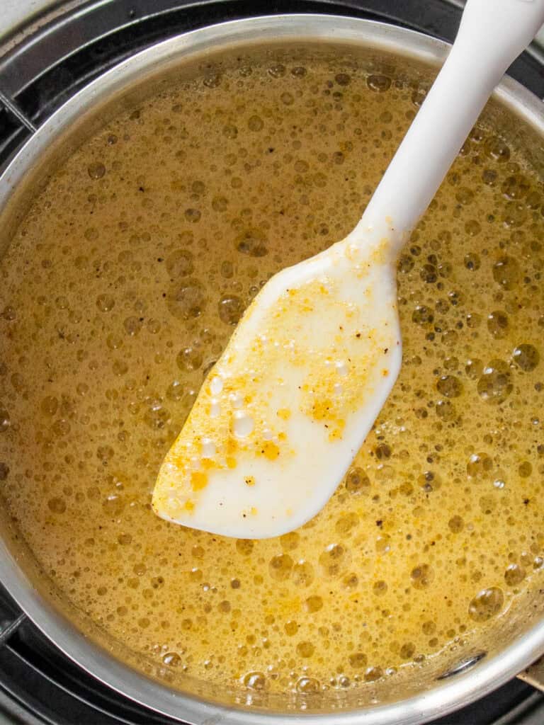 A white spatula stirring a pot of golden, bubbly butter with specks of seasoning.