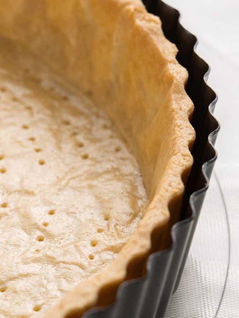 Close-up of an unbaked pie crust in a fluted tart pan, with fork holes pricked into the dough.