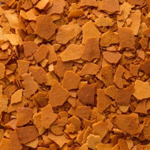 Close-up of scattered golden-brown flakes, resembling baked cereal or pastry pieces, creating a textured surface.