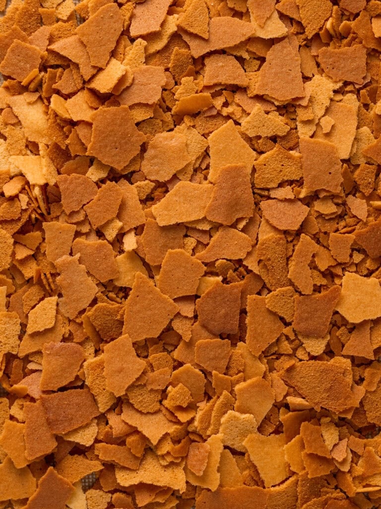 Close-up of a scattered layer of golden brown, crispy flakes, resembling breakfast cereal or baked food pieces, covering the entire image in an irregular, textured pattern.