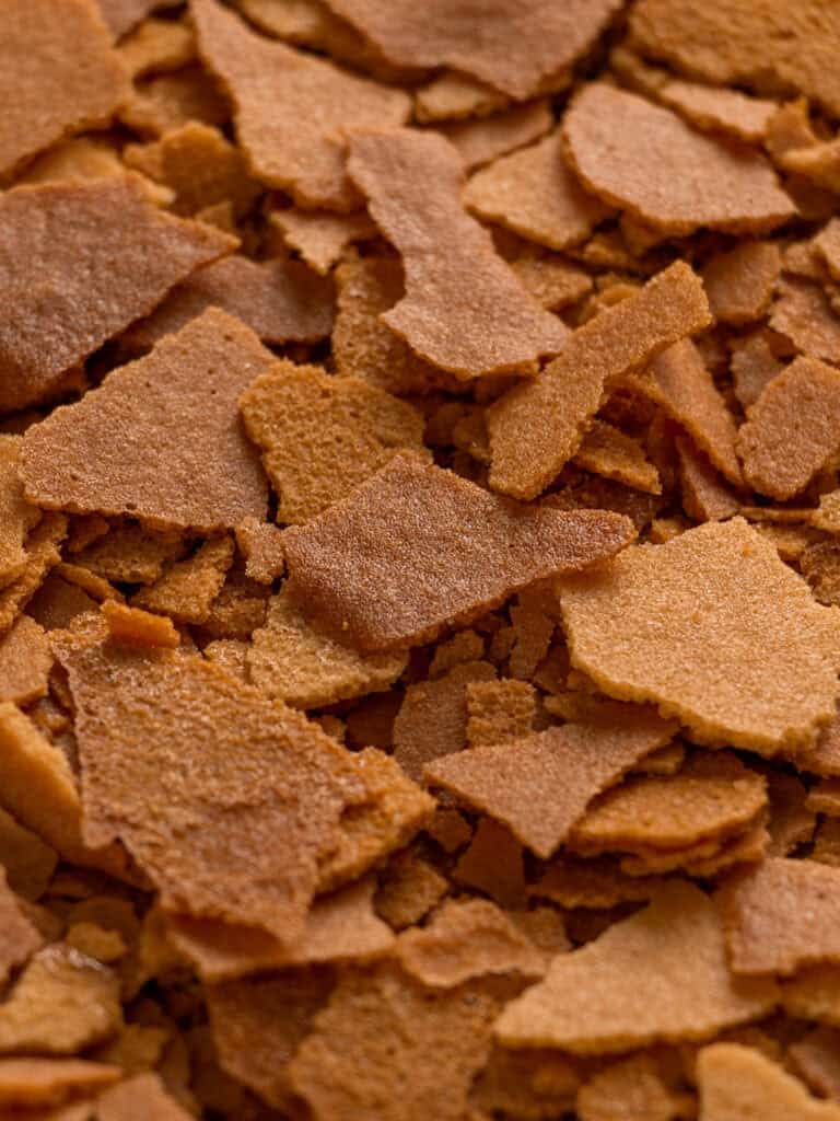 Close-up of golden brown, crispy, irregular flakes scattered in a pile, showing a crunchy texture and slight color variation.