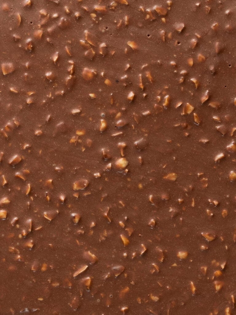 Close-up of milk chocolate embedded with small pieces of chopped nuts.
